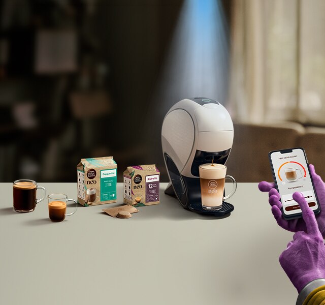 Una mano aliena che usa l'app NESCAFÉ Dolce Gusto per personalizzare un caffè. Macchina da caffè NEO Latte, confezione di caffè e bevande.