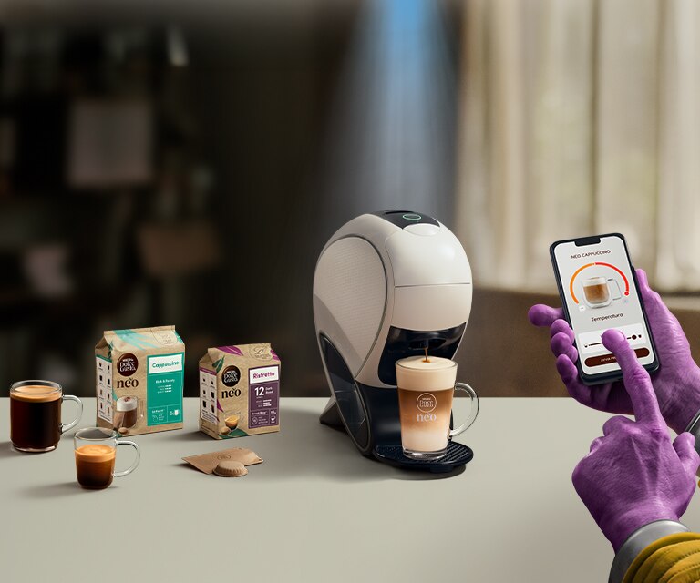 Una mano aliena che usa l'app NESCAFÉ Dolce Gusto per personalizzare un caffè. Macchina da caffè NEO Latte, confezione di caffè e bevande.