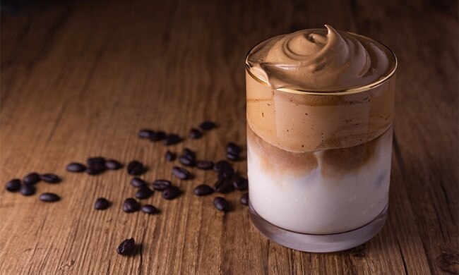 Bicchiere di crema al caffè sul tavolo con chicchi di caffè sparsi accanto