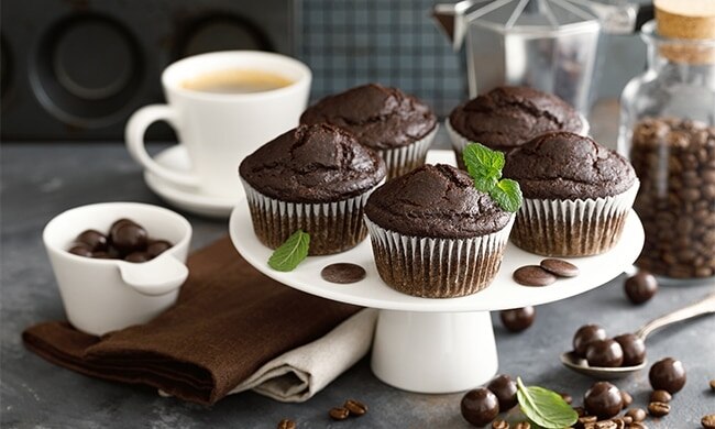 Muffin al caffè su alzatina bianca in tavola con chicchi di caffè e cioccolato accanto