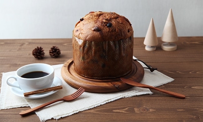 Panettone su base di legno con accanto tazza di caffè Nescafé Dolce Gusto, forchetta, coltello e guarnizioni natalizie