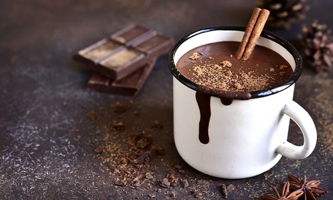 Tazza bianca con cioccolata calda sul tavolo con pezzi di cioccolato accanto